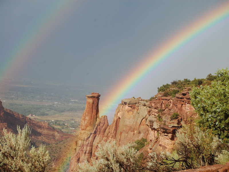 a double rainbow appears over a sparsley vegetated desert cliffside